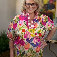 Woman wearing a colorful floral top with a striped collar in an indoor setting.