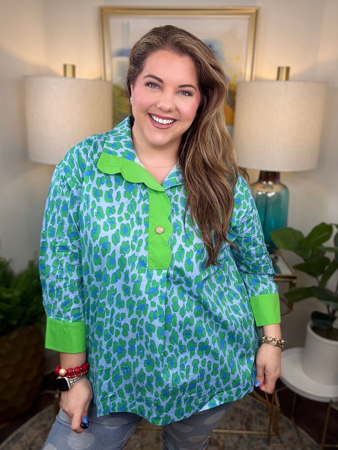 Woman wearing a green and blue patterned shirt in a home setting with lamps and artwork.