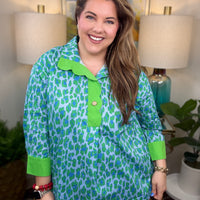 Woman wearing a green and blue patterned shirt in a home setting with lamps and artwork.