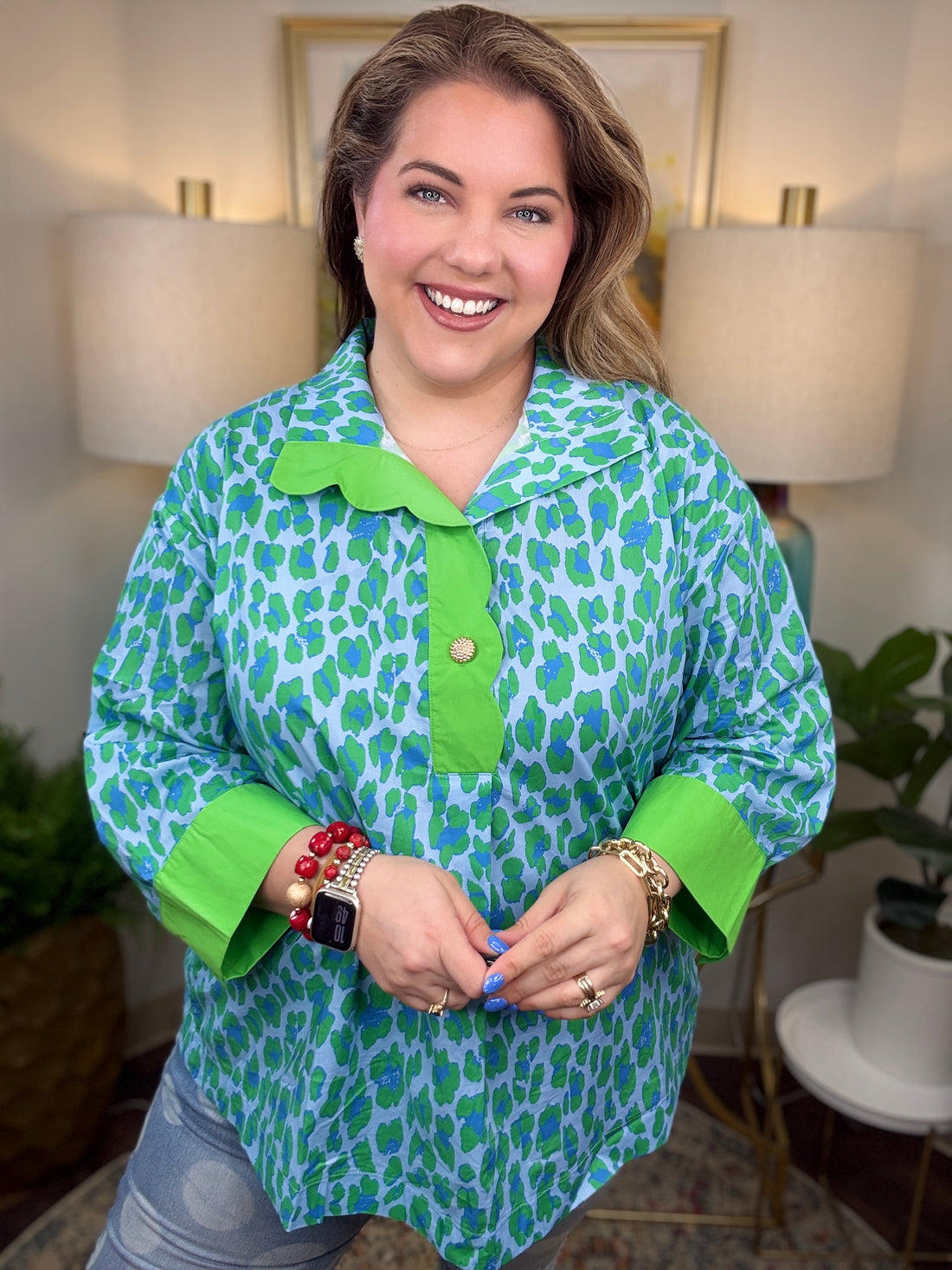Woman wearing a green and blue patterned shirt in a home setting with lamps and artwork.