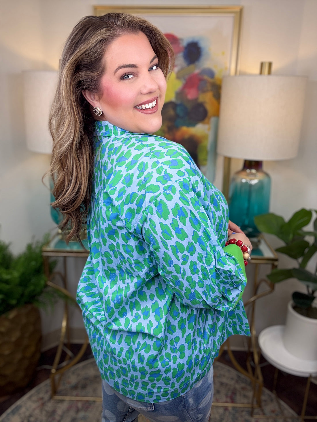 Woman wearing a green and blue patterned shirt in a home setting with lamps and artwork.
