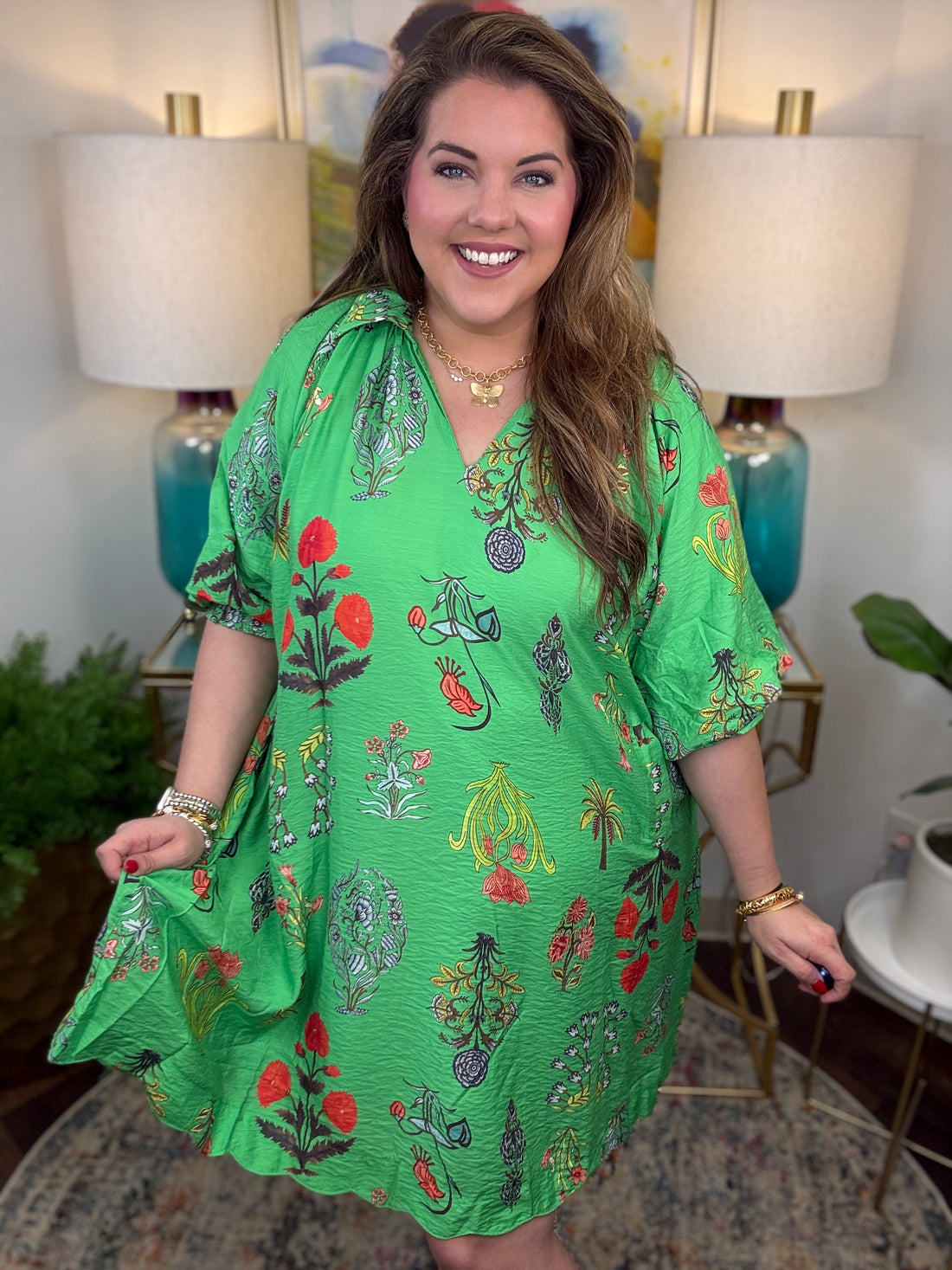 Woman wearing a green floral dress in a home setting with lamps and decor.