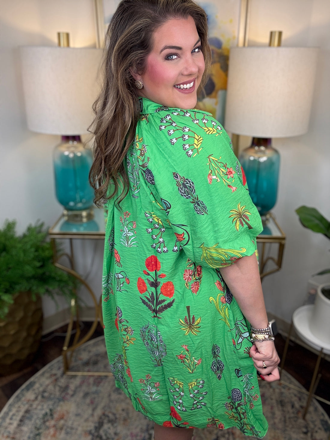 Woman wearing a green floral dress in a home setting with lamps and decor.