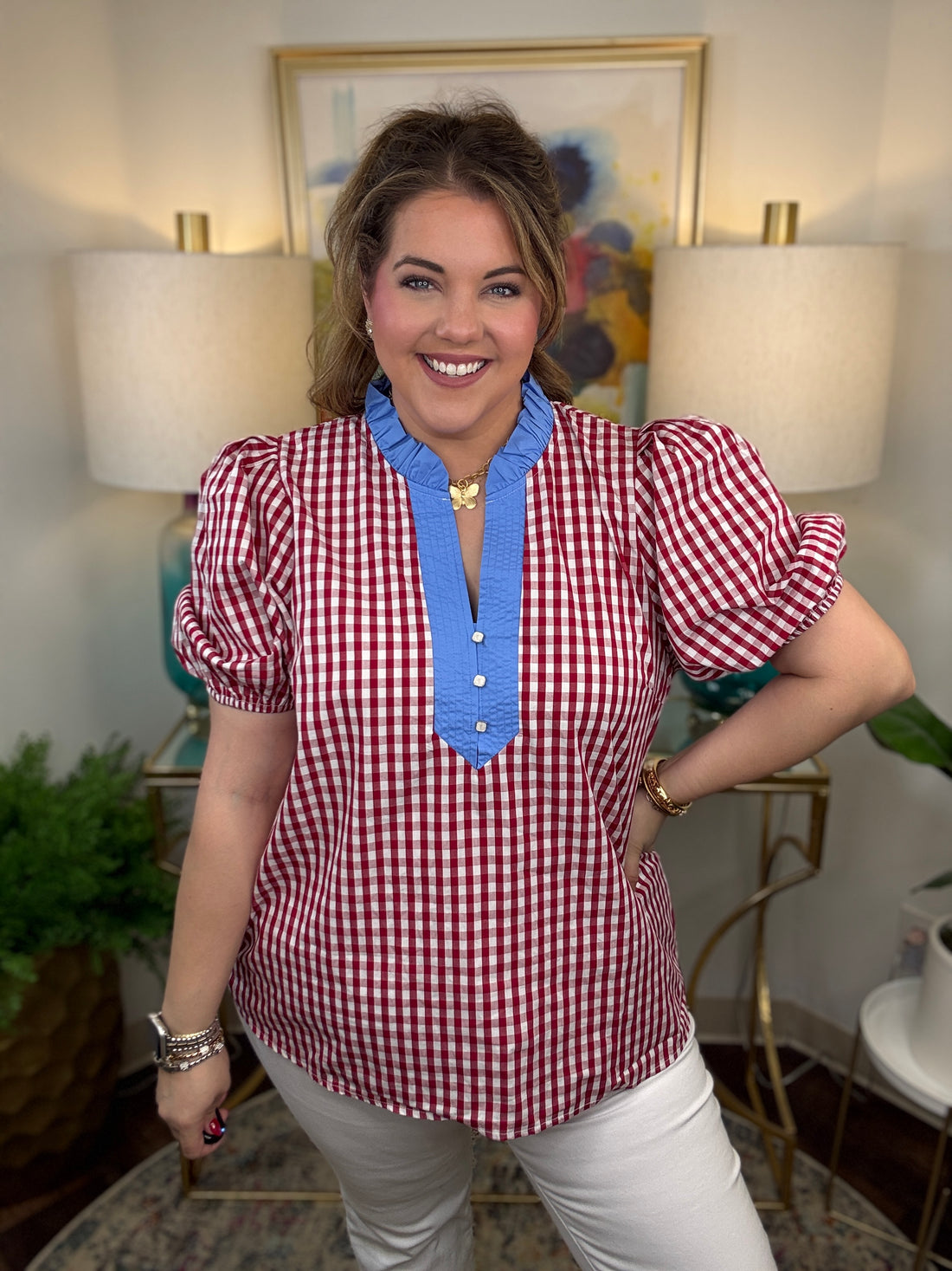 Woman wearing a red and white checkered blouse with blue trim in a room with lamps and artwork.