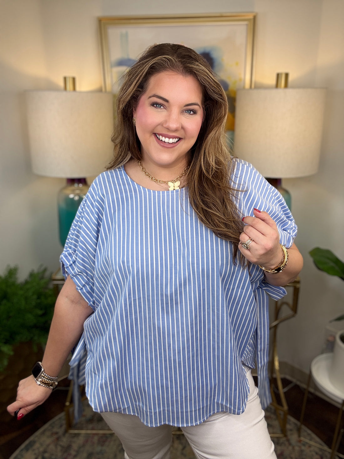 Woman wearing a blue striped shirt in a room with lamps and a painting.