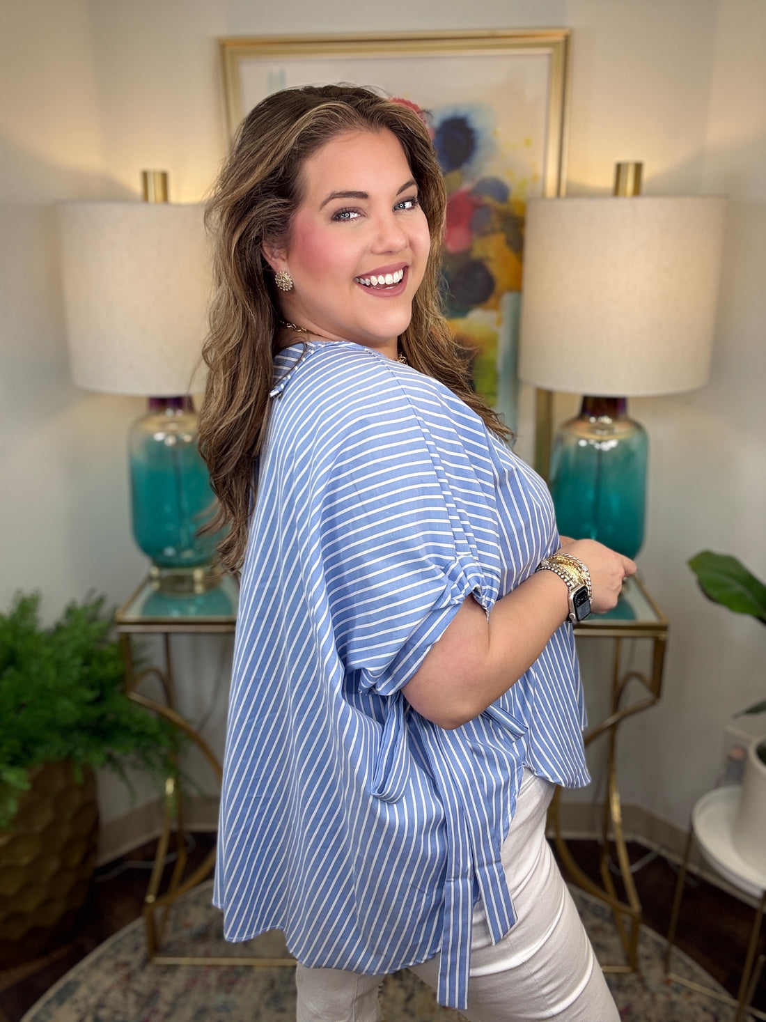 Woman in a blue striped shirt standing in a room with lamps and artwork.