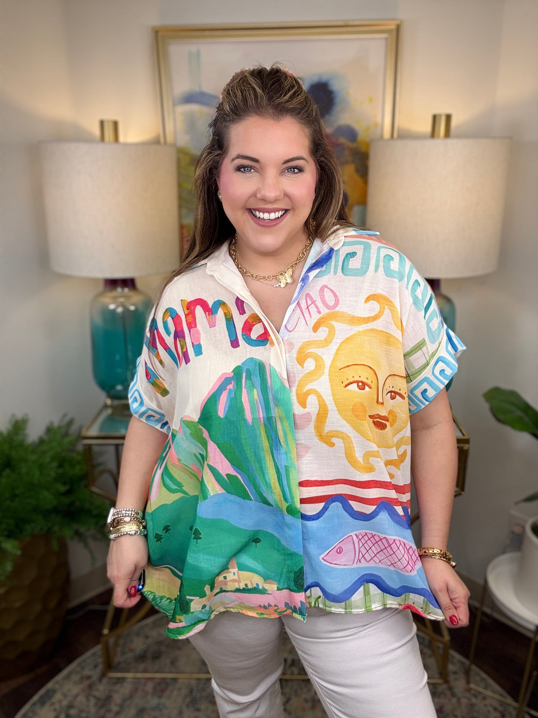 Woman wearing a colorful shirt with artistic designs in a room with lamps and a painting.