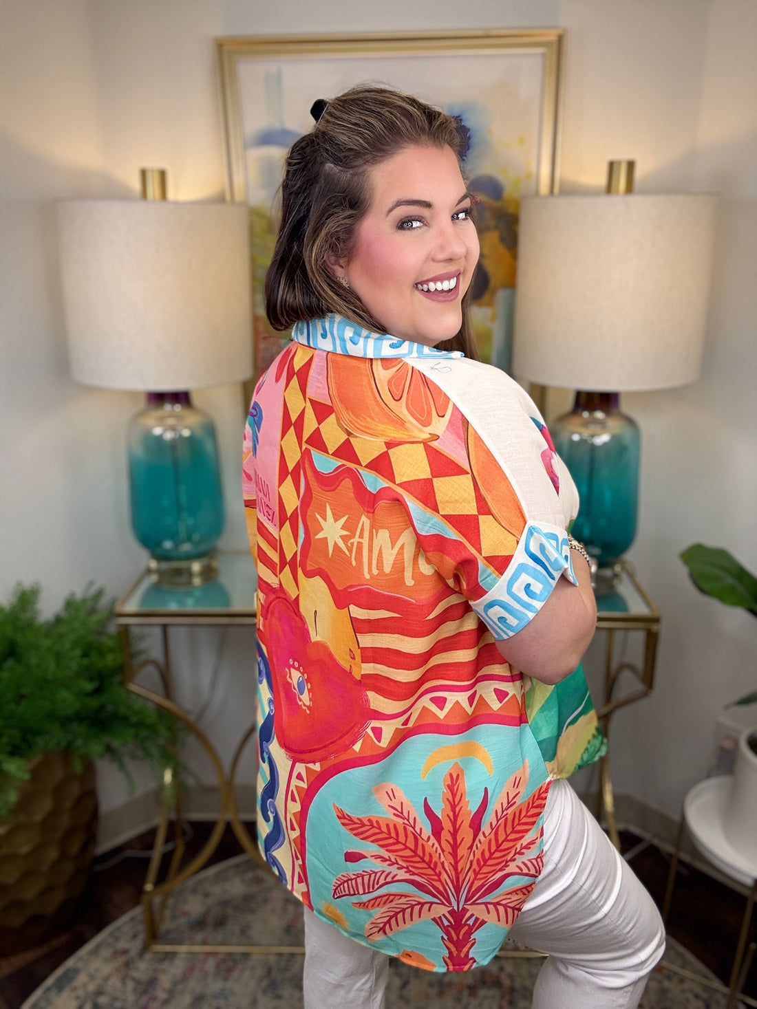 Person wearing a colorful patterned shirt in a room with lamps and a painting.