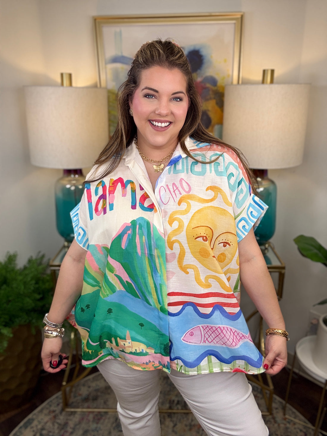 Woman wearing a colorful shirt with artistic designs in a room with lamps and artwork.