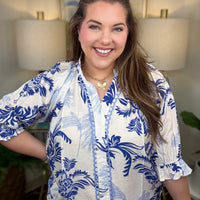Woman wearing a blue and white patterned blouse indoors with lamps and a painting in the background.
