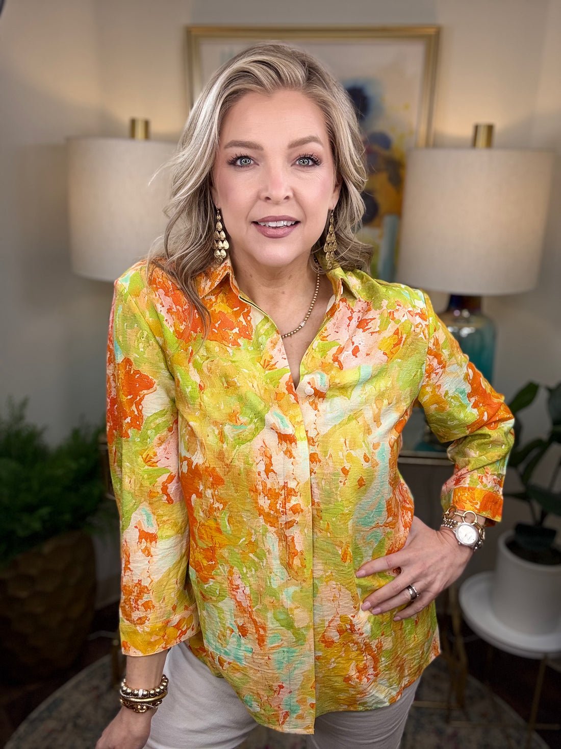 Woman wearing a colorful floral blouse in an indoor setting with lamps and plants.