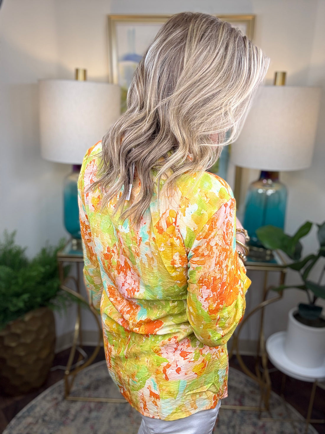 Person wearing a colorful floral blouse in a home setting with lamps and plants.