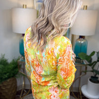 Person wearing a colorful floral blouse in a home setting with lamps and plants.