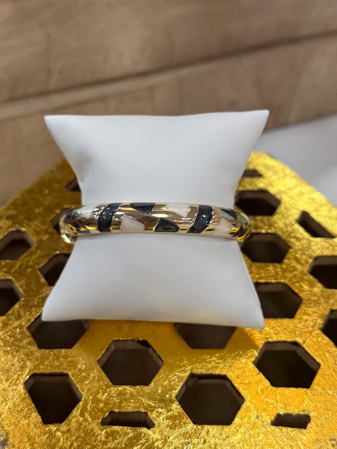 Gold bracelet with black and white pattern on a white cushion against a textured gold background