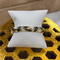 Gold bracelet with black and white pattern on a white cushion against a textured gold background