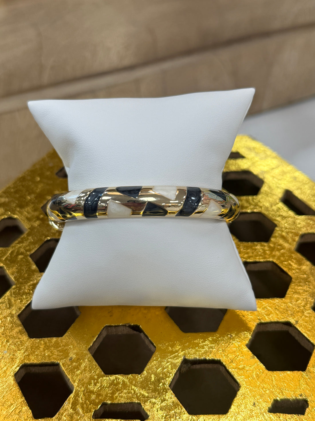 Bangle on a white stand with a gold and black pattern against a textured yellow background