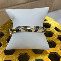 Bangle on a white stand with a gold and black pattern against a textured yellow background