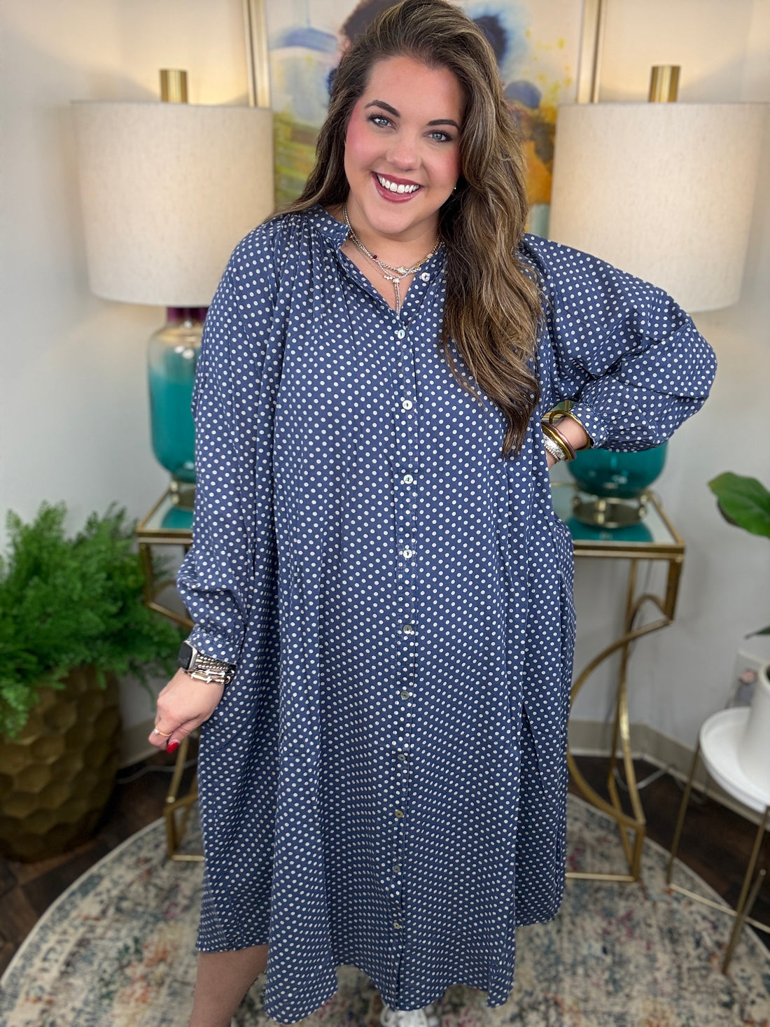 Woman wearing a blue polka dot dress in a home setting with lamps and decor.