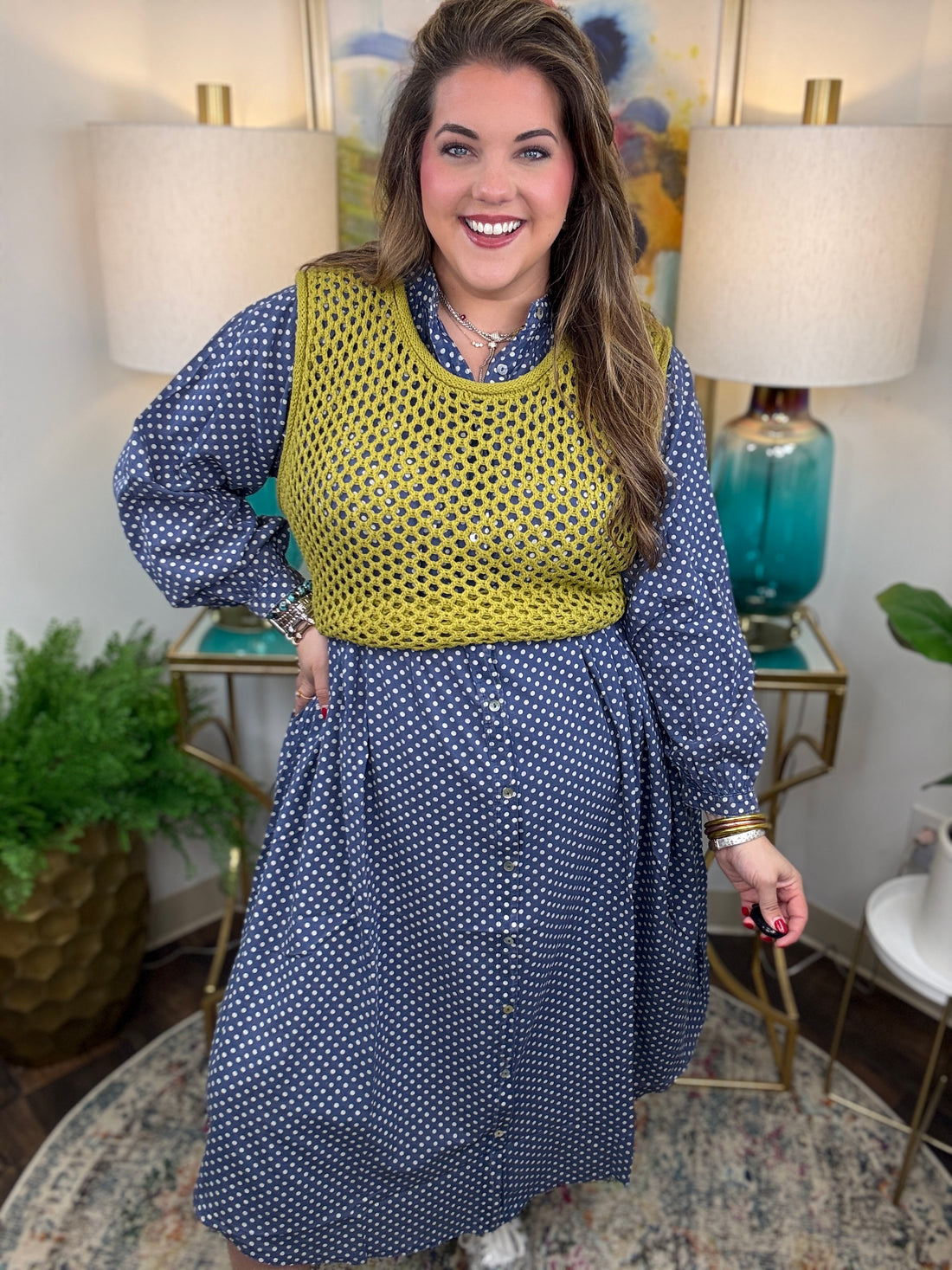 Woman wearing a blue polka dot dress with a yellow top in a home setting.