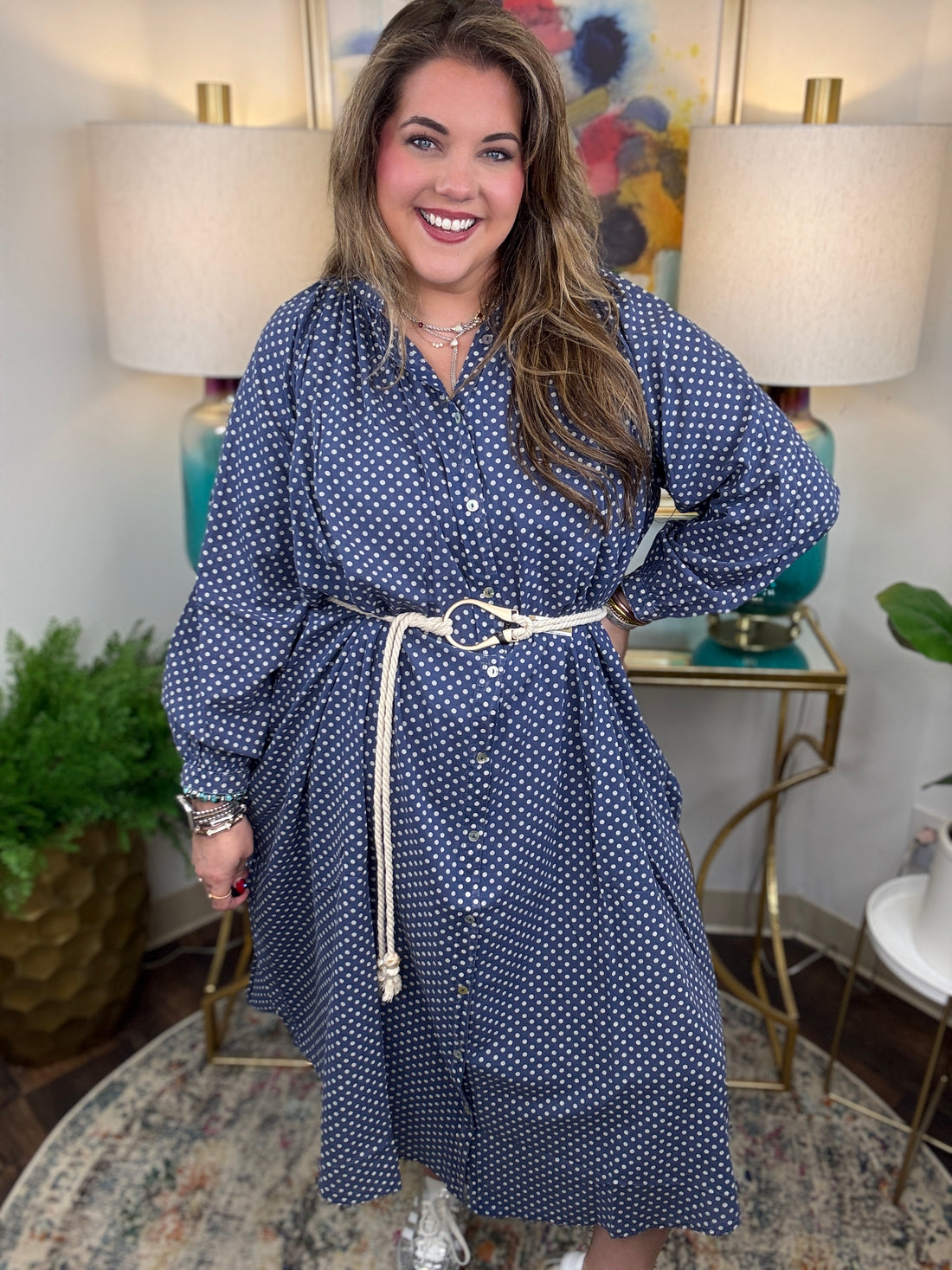Woman wearing a blue polka dot dress in a home setting with lamps and decor.