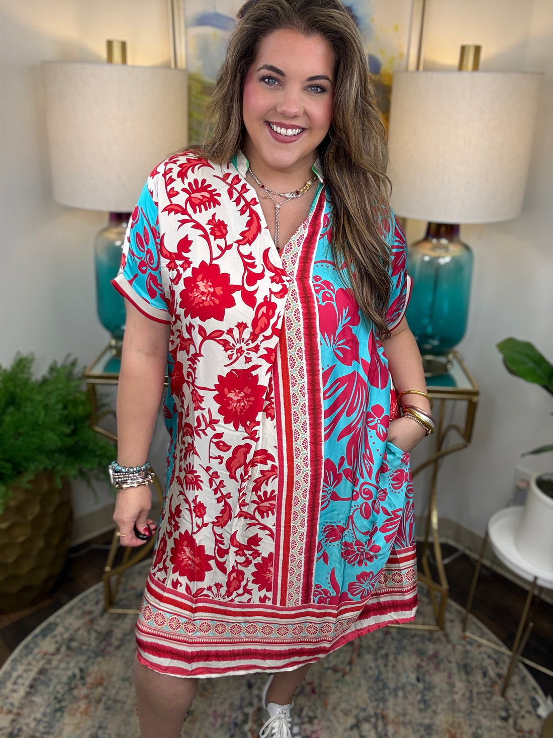 Woman wearing a red and blue floral dress in a home setting with lamps and plants.