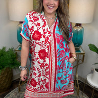 Woman wearing a red and blue floral dress in a home setting with lamps and plants.