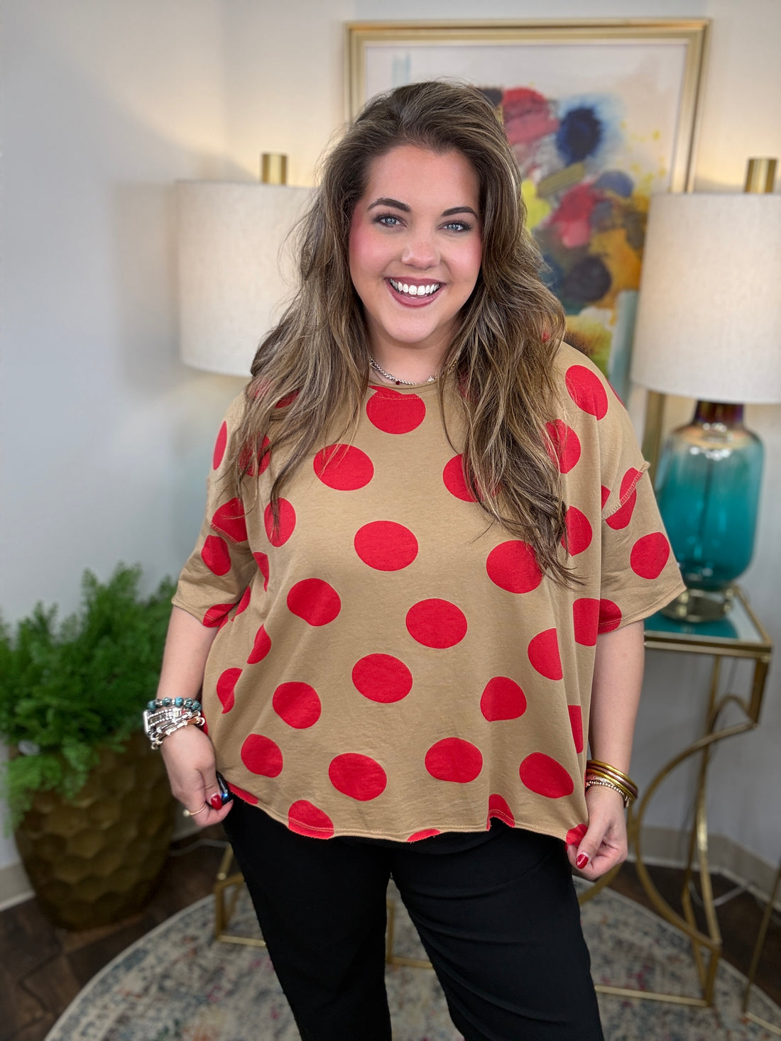 Woman wearing a beige shirt with red polka dots in a room with lamps and a painting.