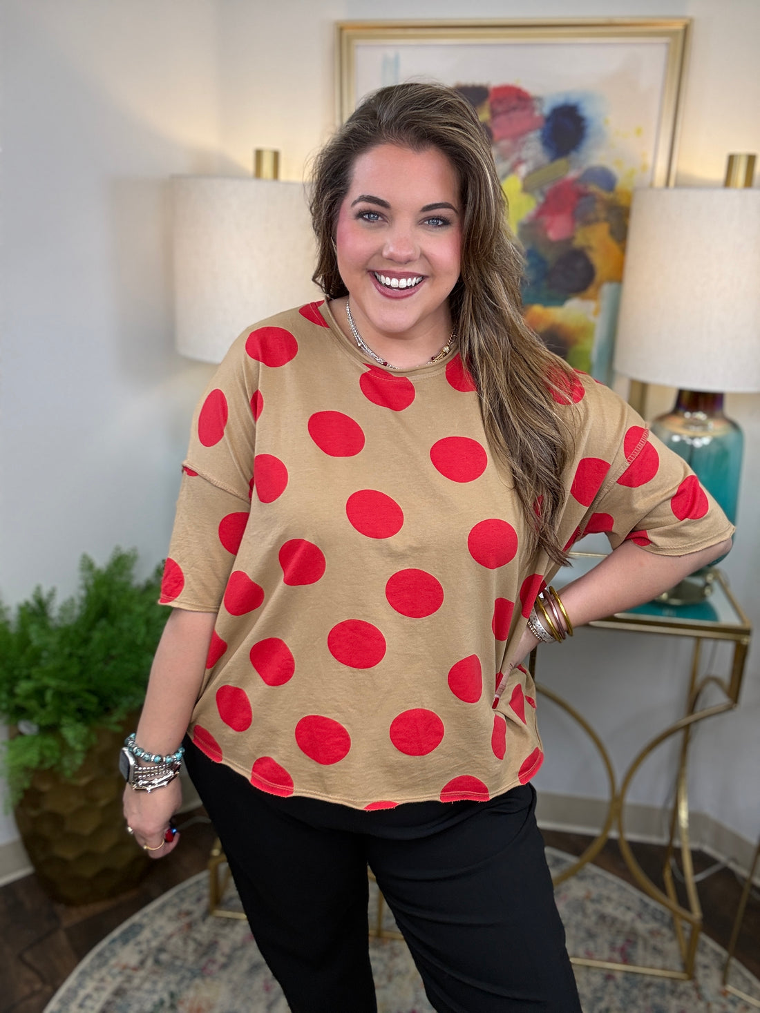 Woman wearing a beige shirt with red polka dots in a room with lamps and a painting.