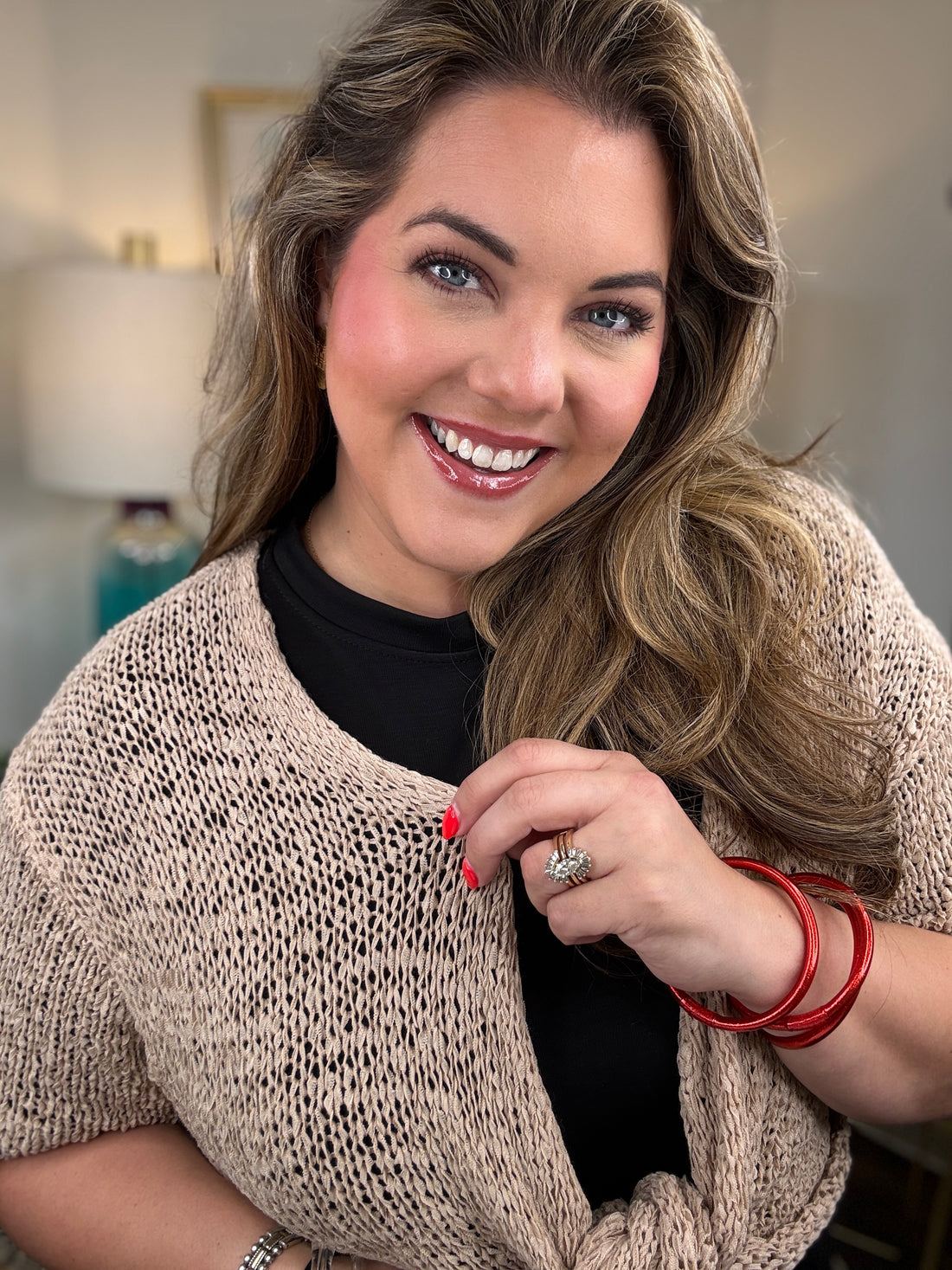 A woman modeling a short-sleeve knit wrap in a warm beige/cream color tied at the waist over a black dress
