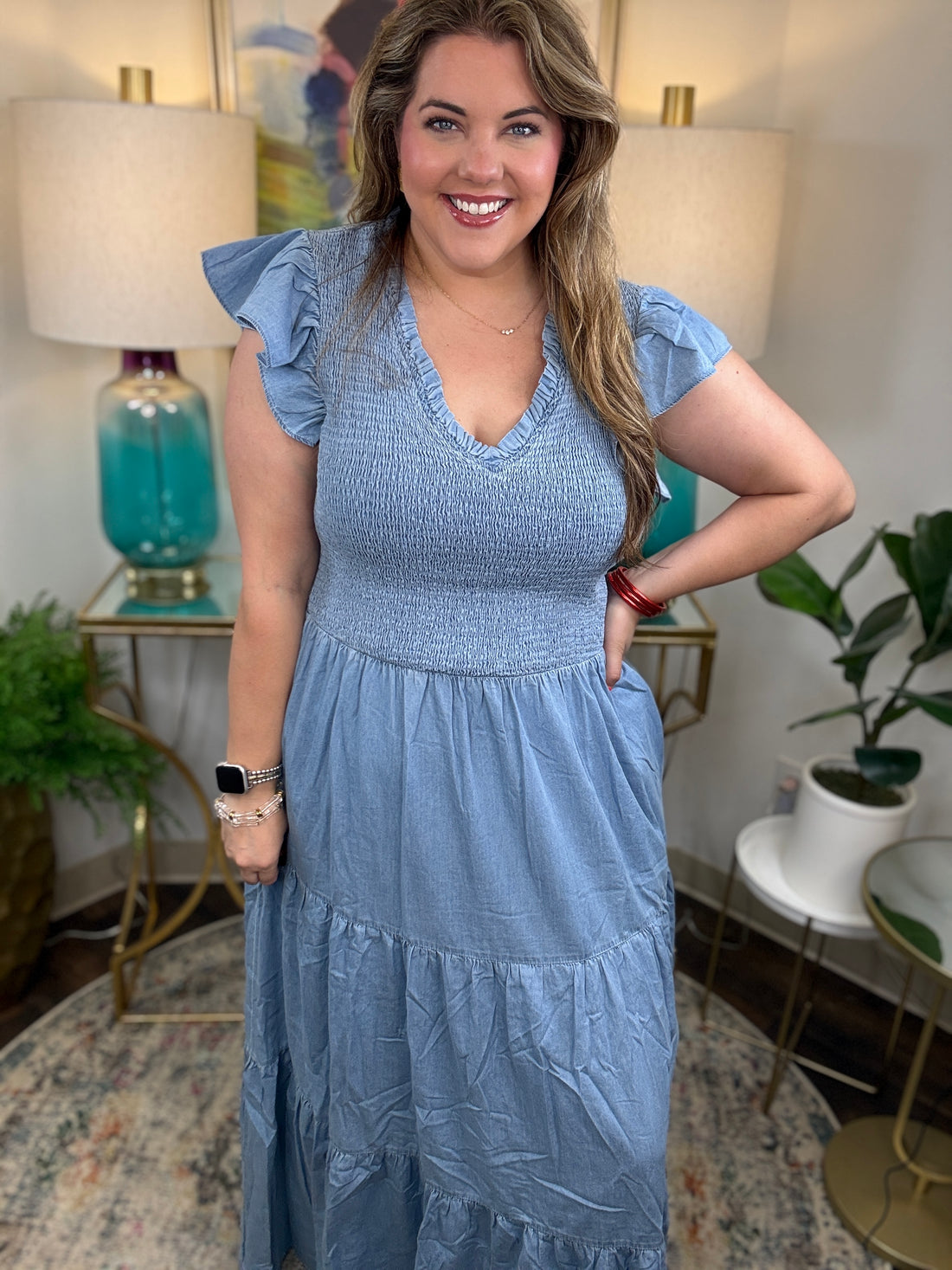 A woman wearing a light blue denim maxi dress with a smocked bodice and short ruffled sleeves