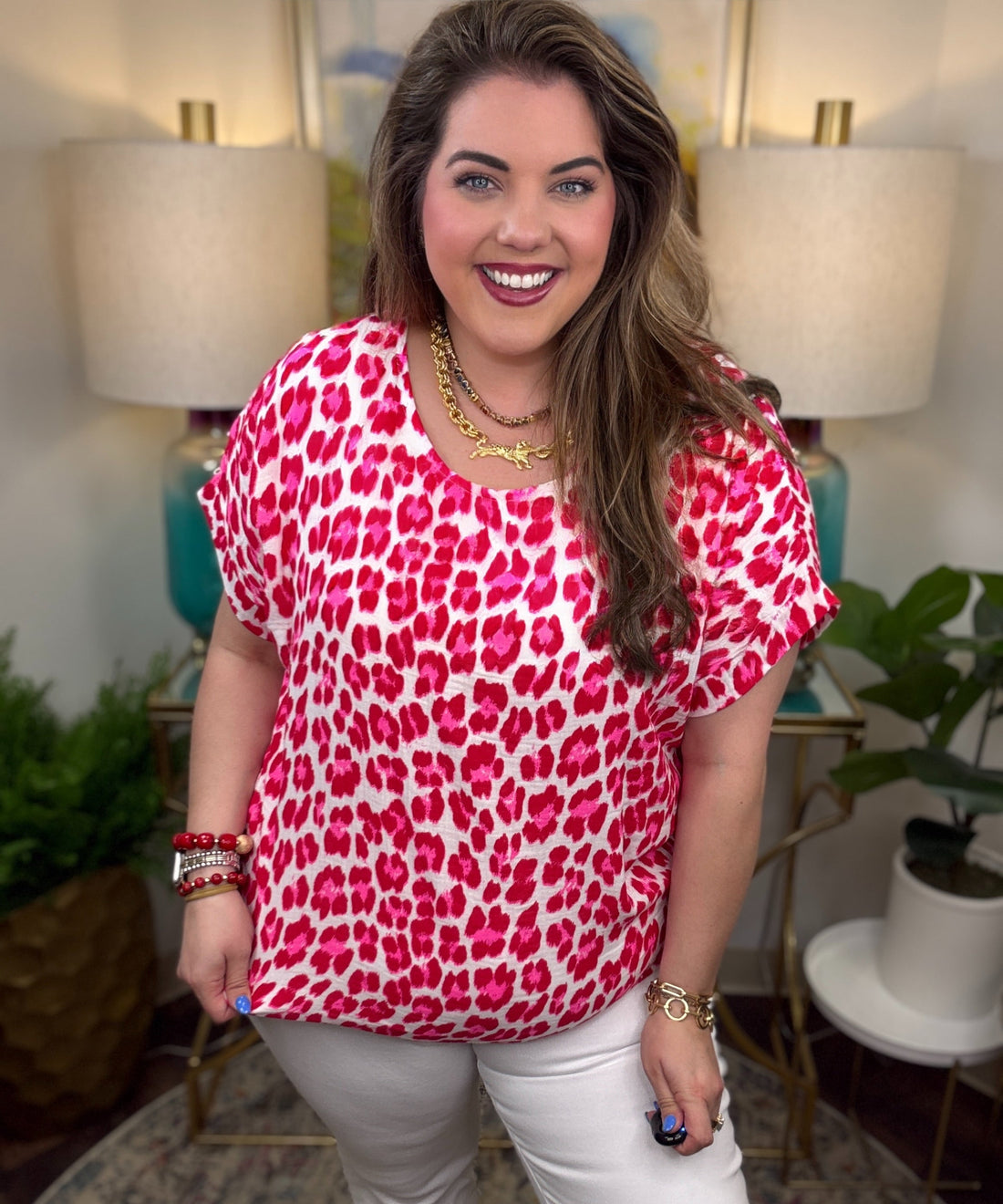 Woman wearing a pink leopard print top and white pants in a home setting.